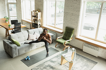 Image showing Young african-american man training at home during quarantine of coronavirus outbreak, doinc exercises of fitness, aerobic. Staying sportive suring insulation.