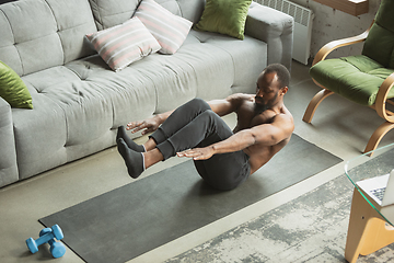 Image showing Young african-american man training at home during quarantine of coronavirus outbreak, doinc exercises of fitness, aerobic. Staying sportive suring insulation.