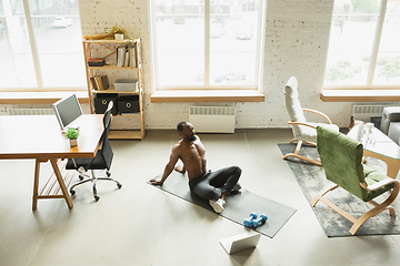 Image showing Young african-american man training at home during quarantine of coronavirus outbreak, doinc exercises of fitness, aerobic. Staying sportive suring insulation.