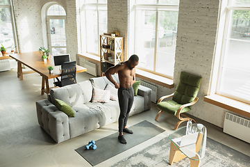 Image showing Young african-american man training at home during quarantine of coronavirus outbreak, doinc exercises of fitness, aerobic. Staying sportive suring insulation.