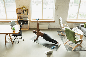 Image showing Young african-american man training at home during quarantine of coronavirus outbreak, doinc exercises of fitness, aerobic. Staying sportive suring insulation.