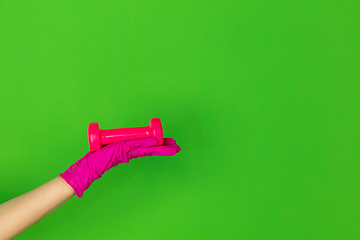 Image showing Hand in pink rubber glove holding gym weight, dumbbell isolated on green studio background with copyspace.