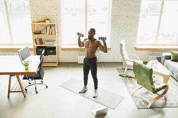 Image showing Young african-american man training at home during quarantine of coronavirus outbreak, doinc exercises of fitness, aerobic. Staying sportive suring insulation.