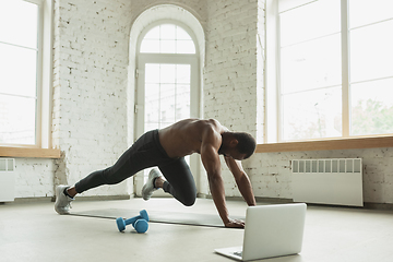 Image showing Young african-american man training at home during quarantine of coronavirus outbreak, doinc exercises of fitness, aerobic. Staying sportive suring insulation.