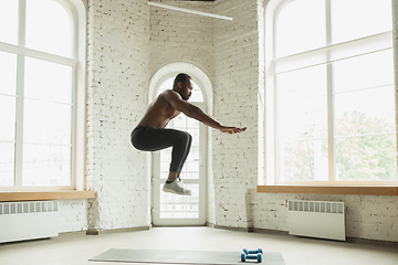 Image showing Young african-american man training at home during quarantine of coronavirus outbreak, doinc exercises of fitness, aerobic. Staying sportive suring insulation.