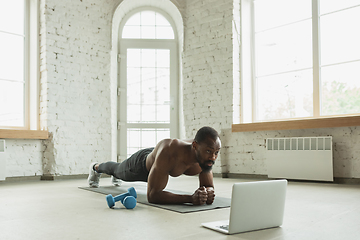 Image showing Young african-american man training at home during quarantine of coronavirus outbreak, doinc exercises of fitness, aerobic. Staying sportive suring insulation.