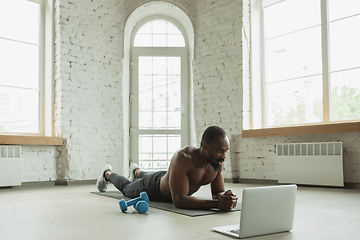 Image showing Young african-american man training at home during quarantine of coronavirus outbreak, doinc exercises of fitness, aerobic. Staying sportive suring insulation.