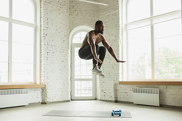 Image showing Young african-american man training at home during quarantine of coronavirus outbreak, doinc exercises of fitness, aerobic. Staying sportive suring insulation.