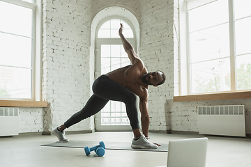 Image showing Young african-american man training at home during quarantine of coronavirus outbreak, doinc exercises of fitness, aerobic. Staying sportive suring insulation.