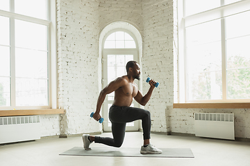 Image showing Young african-american man training at home during quarantine of coronavirus outbreak, doinc exercises of fitness, aerobic. Staying sportive suring insulation.