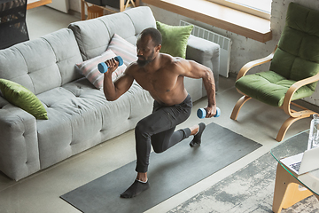 Image showing Young african-american man training at home during quarantine of coronavirus outbreak, doinc exercises of fitness, aerobic. Staying sportive suring insulation.