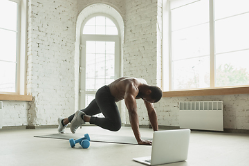 Image showing Young african-american man training at home during quarantine of coronavirus outbreak, doinc exercises of fitness, aerobic. Staying sportive suring insulation.