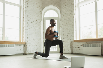 Image showing Young african-american man training at home during quarantine of coronavirus outbreak, doinc exercises of fitness, aerobic. Staying sportive suring insulation.