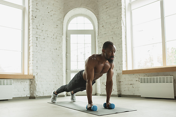 Image showing Young african-american man training at home during quarantine of coronavirus outbreak, doinc exercises of fitness, aerobic. Staying sportive suring insulation.