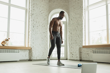 Image showing Young african-american man training at home during quarantine of coronavirus outbreak, doinc exercises of fitness, aerobic. Staying sportive suring insulation.