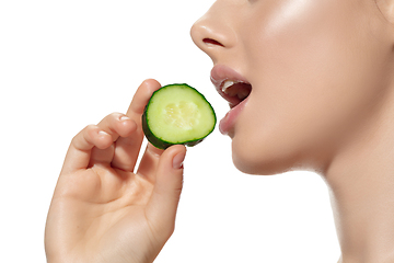 Image showing Freshness. Close up of beautiful young woman biting cucumber\'s slice over white background. Cosmetics and makeup, natural and eco treatment, skin care.