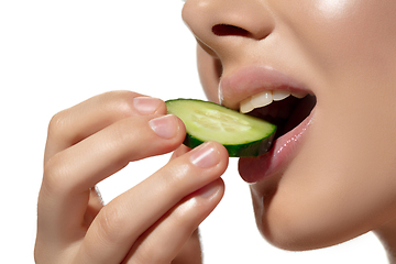Image showing Freshness. Close up of beautiful young woman biting cucumber\'s slice over white background. Cosmetics and makeup, natural and eco treatment, skin care.