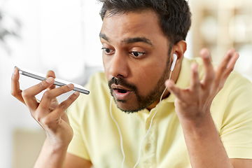 Image showing angry man with earphones calling on smartphone