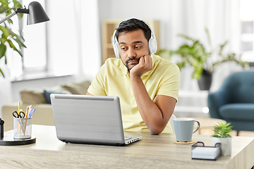 Image showing bored man in headphones with laptop works at home