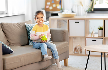 Image showing happy little girl with apple sitting on sofa