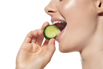 Image showing Freshness. Close up of beautiful young woman biting cucumber\'s slice over white background. Cosmetics and makeup, natural and eco treatment, skin care.