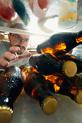 Image showing Caucasian man takes cold refreshing beer from out the fridge, inside view from fridge of hand holding the bottle