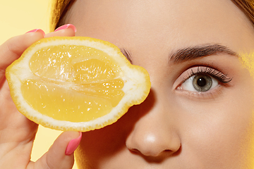 Image showing Close up of beautiful female face with lemon slice over yellow background. Cosmetics and makeup, natural and eco treatment, skin care.