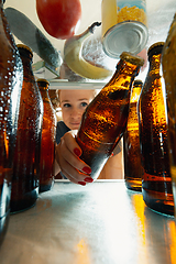 Image showing Caucasian woman takes cold refreshing beer from out the fridge, inside view from fridge of hand holding the bottle