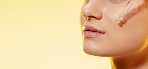 Image showing Close up of beautiful young woman with essential oil pouring over yellow background. Cosmetics and makeup, natural and eco treatment, skin care. Flyer with copyspace.