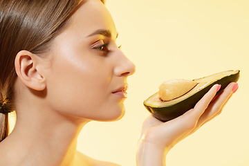 Image showing Close up of beautiful female face with half avocado over yellow background. Cosmetics and makeup, natural and eco treatment, skin care.