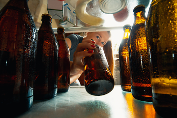 Image showing Caucasian woman takes cold refreshing beer from out the fridge, inside view from fridge of hand holding the bottle