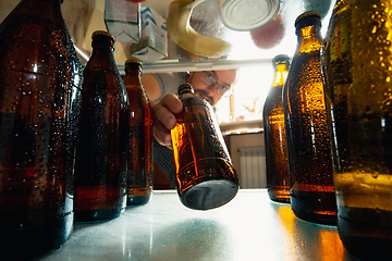 Image showing Caucasian man takes cold refreshing beer from out the fridge, inside view from fridge of hand holding the bottle