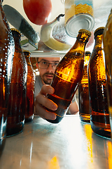 Image showing Caucasian man takes cold refreshing beer from out the fridge, inside view from fridge of hand holding the bottle