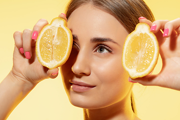 Image showing Close up of beautiful female face with lemon slices over yellow background. Cosmetics and makeup, natural and eco treatment, skin care.