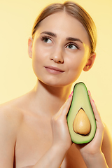 Image showing Organic. Close up of beautiful female face with half avocado over yellow background. Cosmetics and makeup, natural and eco treatment, skin care.