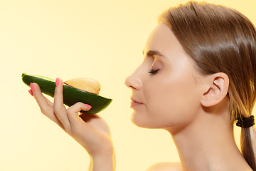 Image showing Organic. Close up of beautiful female face with half avocado over yellow background. Cosmetics and makeup, natural and eco treatment, skin care.