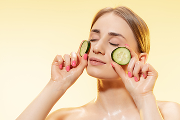 Image showing Green. Close up of beautiful female face with cucumber slices over yellow background. Cosmetics and makeup, natural and eco treatment, skin care.