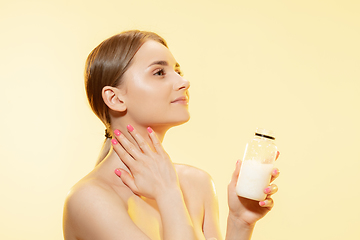 Image showing Shining. Close up of beautiful woman with moisturizer over yellow background. Cosmetics and makeup, natural and eco treatment, skin care.