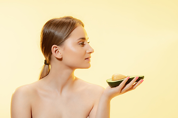 Image showing Fresh. Close up of beautiful female face with half avocado over yellow background. Cosmetics and makeup, natural and eco treatment, skin care.