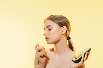 Image showing Vitamins splash. Close up of beautiful female face with lemon and avocado halfs over yellow background. Cosmetics and makeup, natural and eco treatment, skin care.