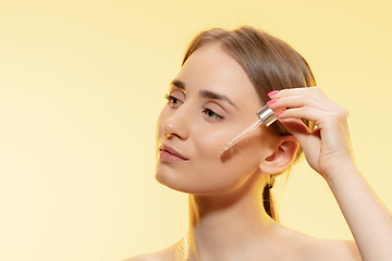Image showing Protection. Close up of beautiful female face with pouring essential oil, serum over yellow background. Cosmetics and makeup, natural and eco treatment, skin care.
