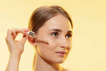 Image showing Protection. Close up of beautiful female face with pouring essential oil, serum over yellow background. Cosmetics and makeup, natural and eco treatment, skin care.