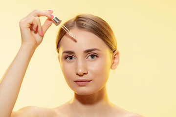 Image showing Protection. Close up of beautiful female face with pouring essential oil, serum over yellow background. Cosmetics and makeup, natural and eco treatment, skin care.