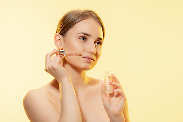 Image showing Nutrition. Close up of beautiful female face with pouring essential oil, serum over yellow background. Cosmetics and makeup, natural and eco treatment, skin care.