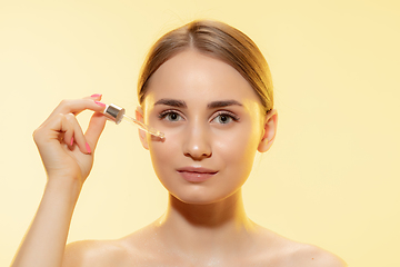 Image showing Nutrition. Close up of beautiful female face with pouring essential oil, serum over yellow background. Cosmetics and makeup, natural and eco treatment, skin care.