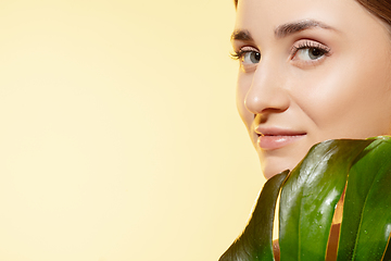 Image showing Look. Close up of beautiful female face with green leaves over white background. Cosmetics and makeup, natural and eco treatment, skin care.