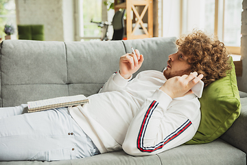 Image showing Manager or student working from home while being insulated or keep quarantine \'cause of coronavirus COVID-19. Listening to voice message lying down on sofa.