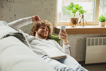 Image showing Manager or student working from home while being insulated or keep quarantine \'cause of coronavirus COVID-19. Scrolling phone lying down on sofa.