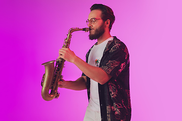 Image showing Young caucasian jazz musician playing the saxophone in neon light