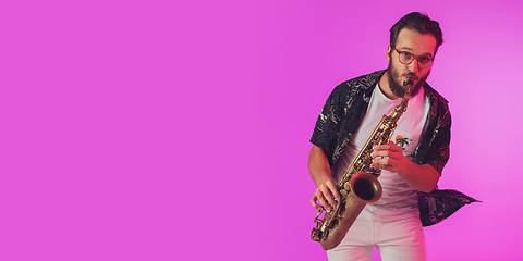 Image showing Young caucasian jazz musician playing the saxophone in neon light, flyer with copyspace for ad